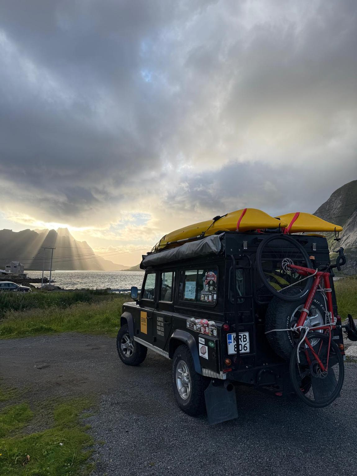 The Beast parked above a fjord in Lofoten at sunset, kayaks on the roof.